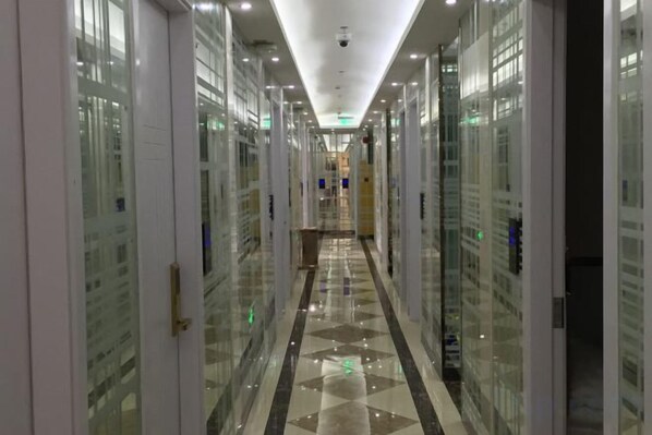 Un pasillo con puertas de cristal que dan a habitaciones, suelo de baldosas e iluminación empotrada en el techo.
