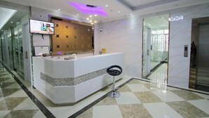 A modern reception area with a white counter, a television mounted above it, and a glass door leading to a hallway. - Shanghai Yajing Business Hotel (Xinhua Hospital Branch) (Shanghai)