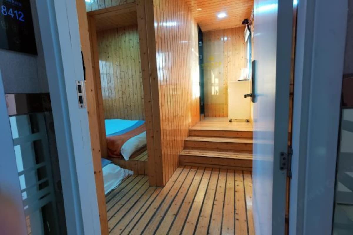 A wooden interior with a bed, a small table, and a staircase leading to a higher level.