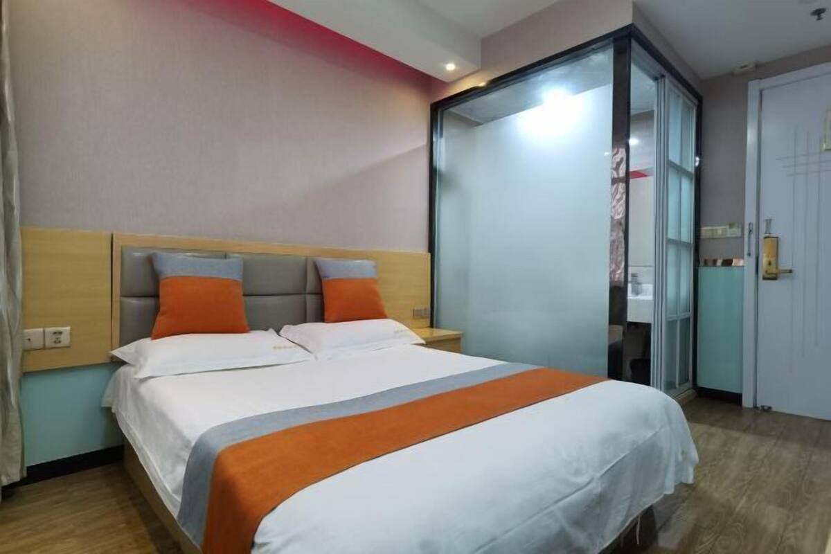 Une chambre d’hôtel avec un lit, des tables de chevet, une porte coulissante et une salle de bain visible.