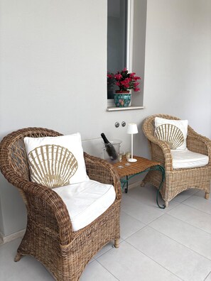Two wicker chairs with white cushions and a small table with a lamp and two glasses.