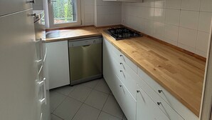 Una cocina con armarios blancos, encimera de madera, lavavajillas, estufa y ventana con vistas a árboles.