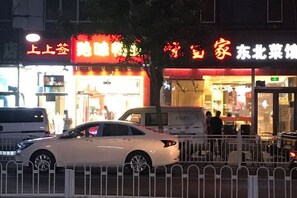A street view with a white car parked in front of a building with illuminated signage. - Beijing Spring Hotel (Beijing)