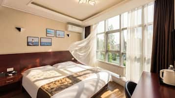 Habitación de hotel con cama, mesita de noche, lámpara y vistas al exterior.