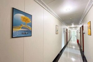A hotel corridor with framed artwork on the walls, a polished floor, and doors leading to rooms. - Beijing Spring Hotel (Beijing)