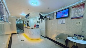 A hotel reception area with a marble counter, a television mounted on the wall, and a seating area with a table and chairs. - Beijing Spring Hotel (Beijing)