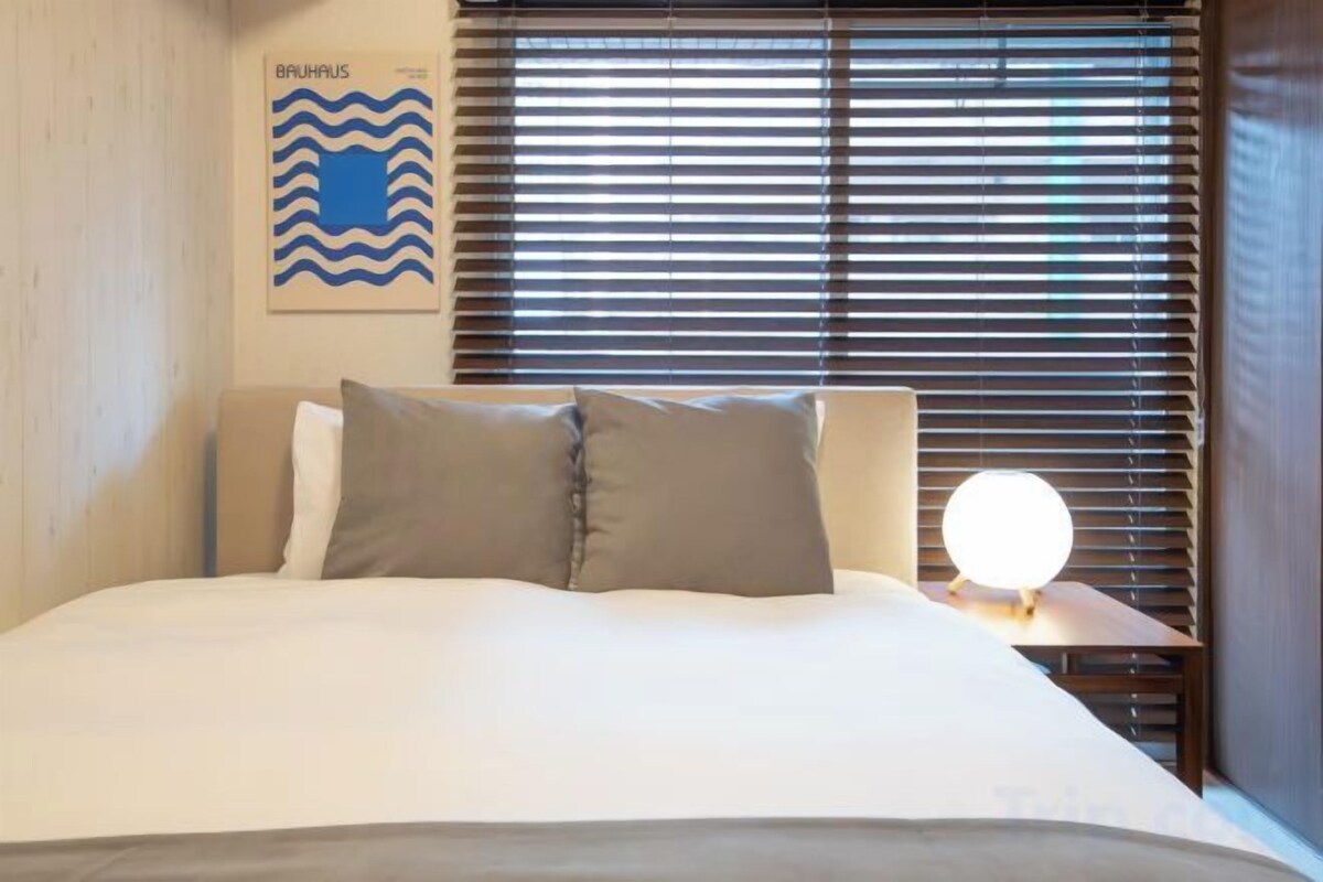 A bed with pillows, a wall-mounted artwork, and a bedside table with a lamp.