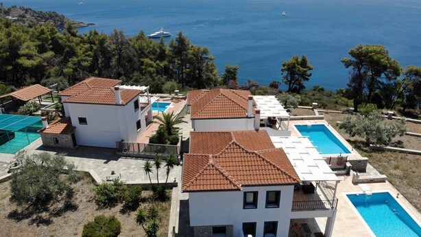 A coastal property with multiple buildings, swimming pools, and a view of the sea.