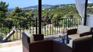 A balcony with wicker furniture and a view of a hilly landscape.