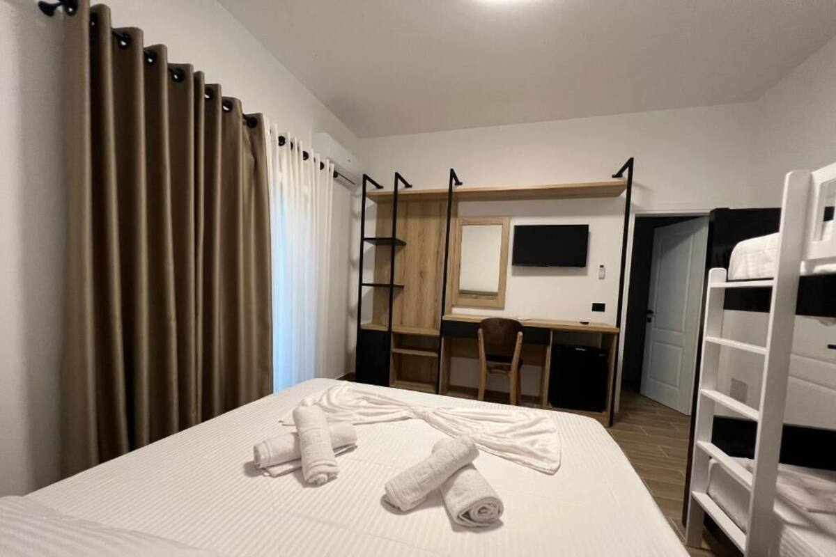 A hotel room with a bed, a desk, a chair, a TV, and a bunk bed.