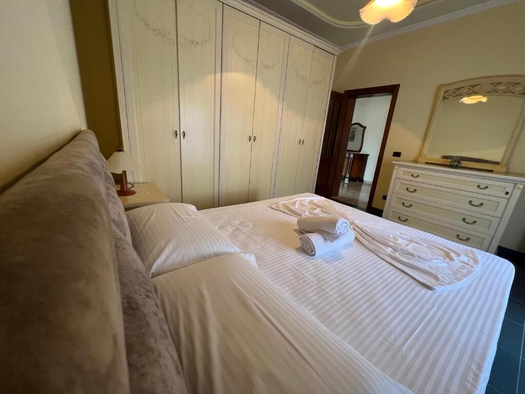 A neatly made bed with white linens, a large wardrobe with multiple doors, and a dresser with drawers.