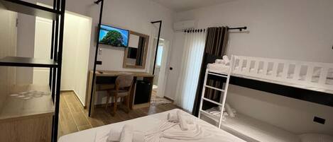 A hotel room with a bed, a desk, a chair, a TV, and a bunk bed.