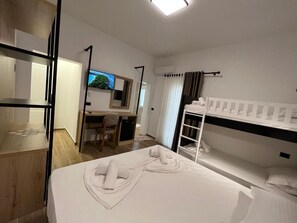 Ein Hotelzimmer mit einem Bett, einem Schreibtisch, einem Stuhl, einem Fernseher und einem Etagenbett.
