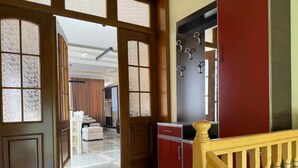 Un hall d’hôtel avec un sol à carreaux, un escalier doté d’une rampe en bois et un mur rouge et noir agrémenté d’un porte-manteau.