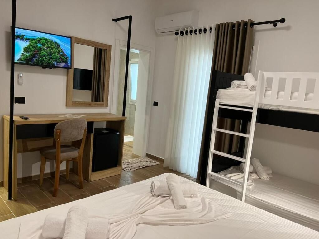 Ein Hotelzimmer mit Bett, Schreibtisch mit Stuhl, Fernseher, Etagenbett und Fenster mit Vorhängen.