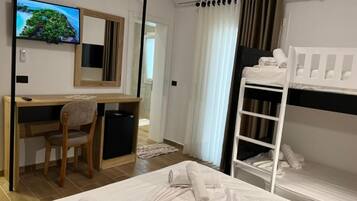 Ein Hotelzimmer mit Bett, Schreibtisch mit Stuhl, Fernseher, Etagenbett und Fenster mit Vorhängen.