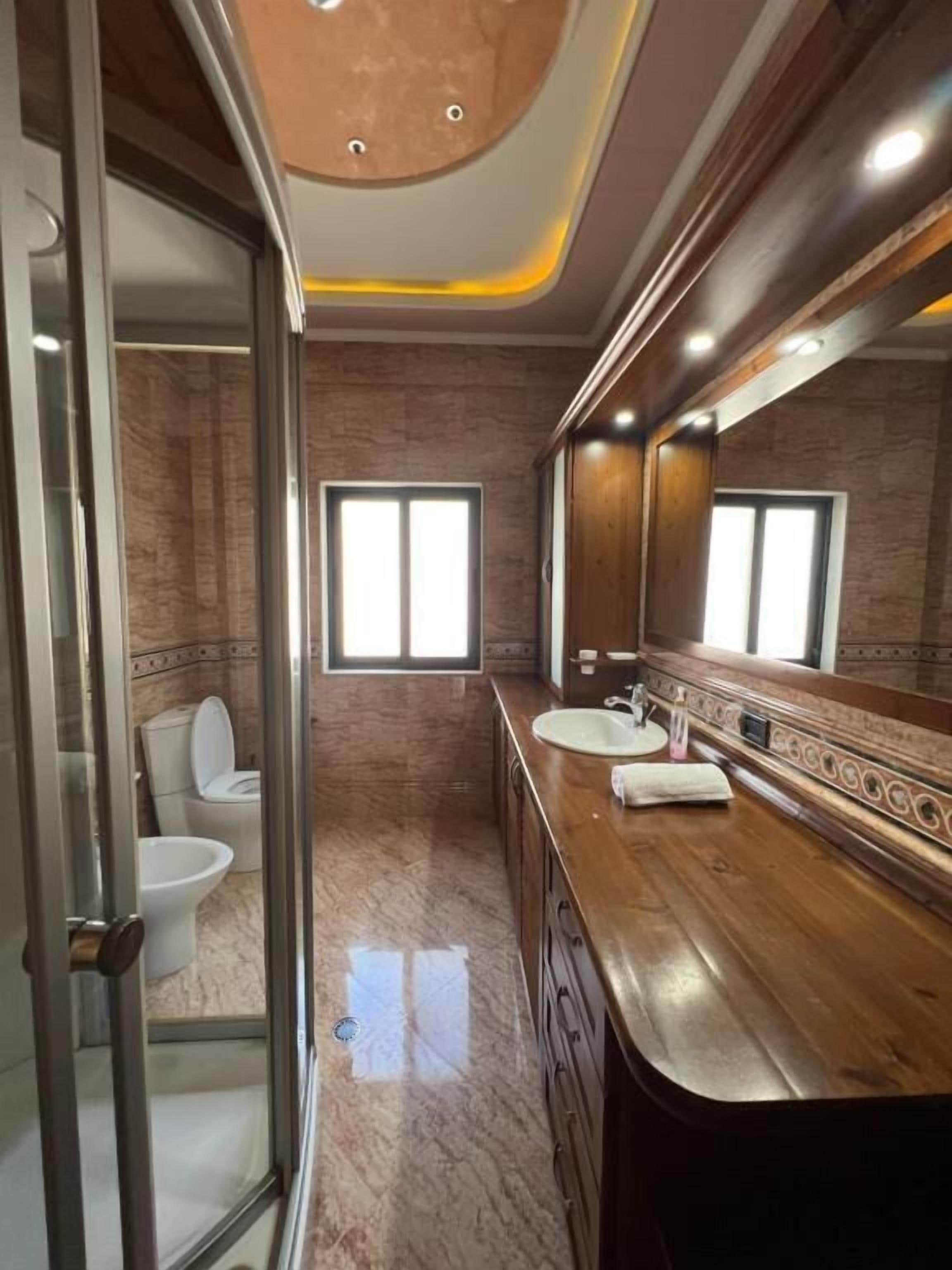 Une salle de bain moderne avec une douche à parois de verre, un meuble-lavabo en bois doté d’un grand miroir et un sol en marbre.