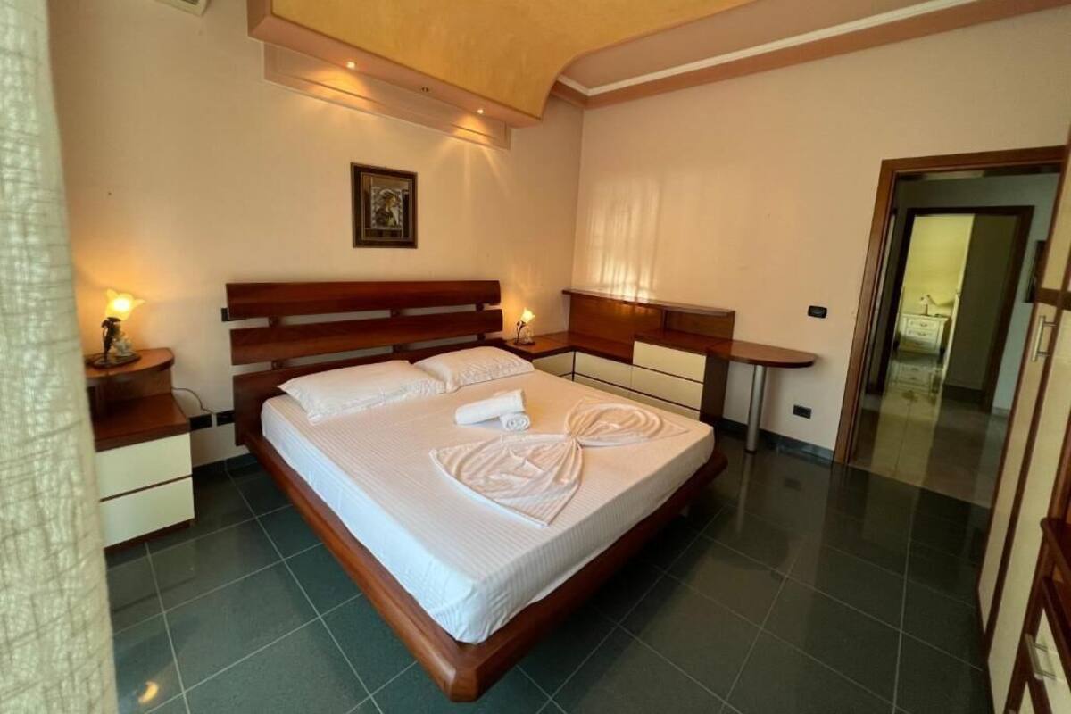 A hotel room with a large bed, wooden headboard, bedside tables, and a small desk.