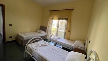 A room with two single beds, a window with curtains, and a ceiling light.