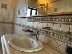 Ein Badezimmer mit einem weißen Waschbecken, einem Spiegel mit dekorativen Fliesen und einem Fenster oberhalb des Spiegels.