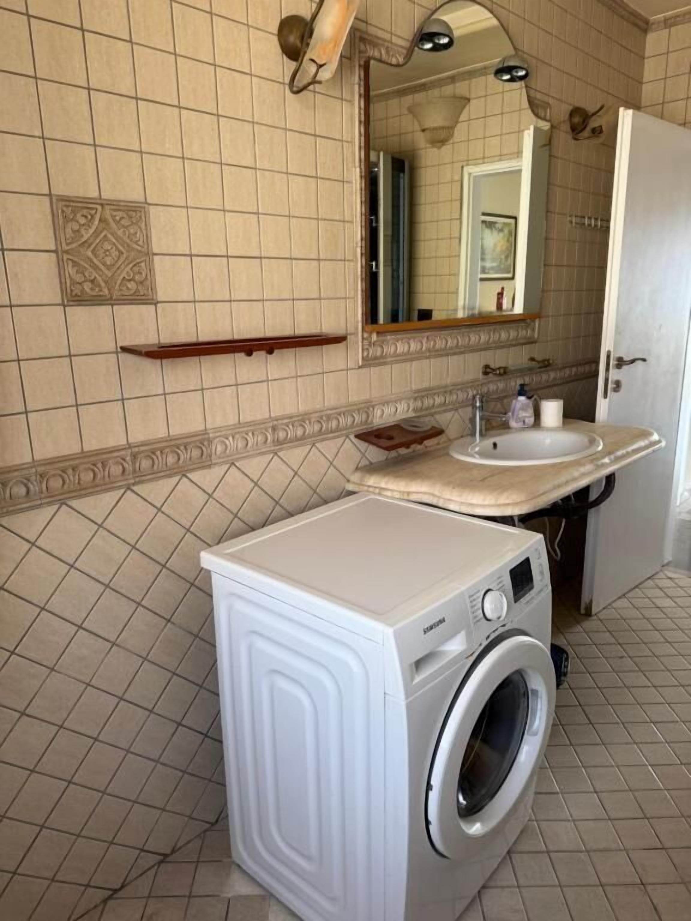 Une salle de bain équipée d’un lave-linge, d’un lavabo et d’un miroir.
