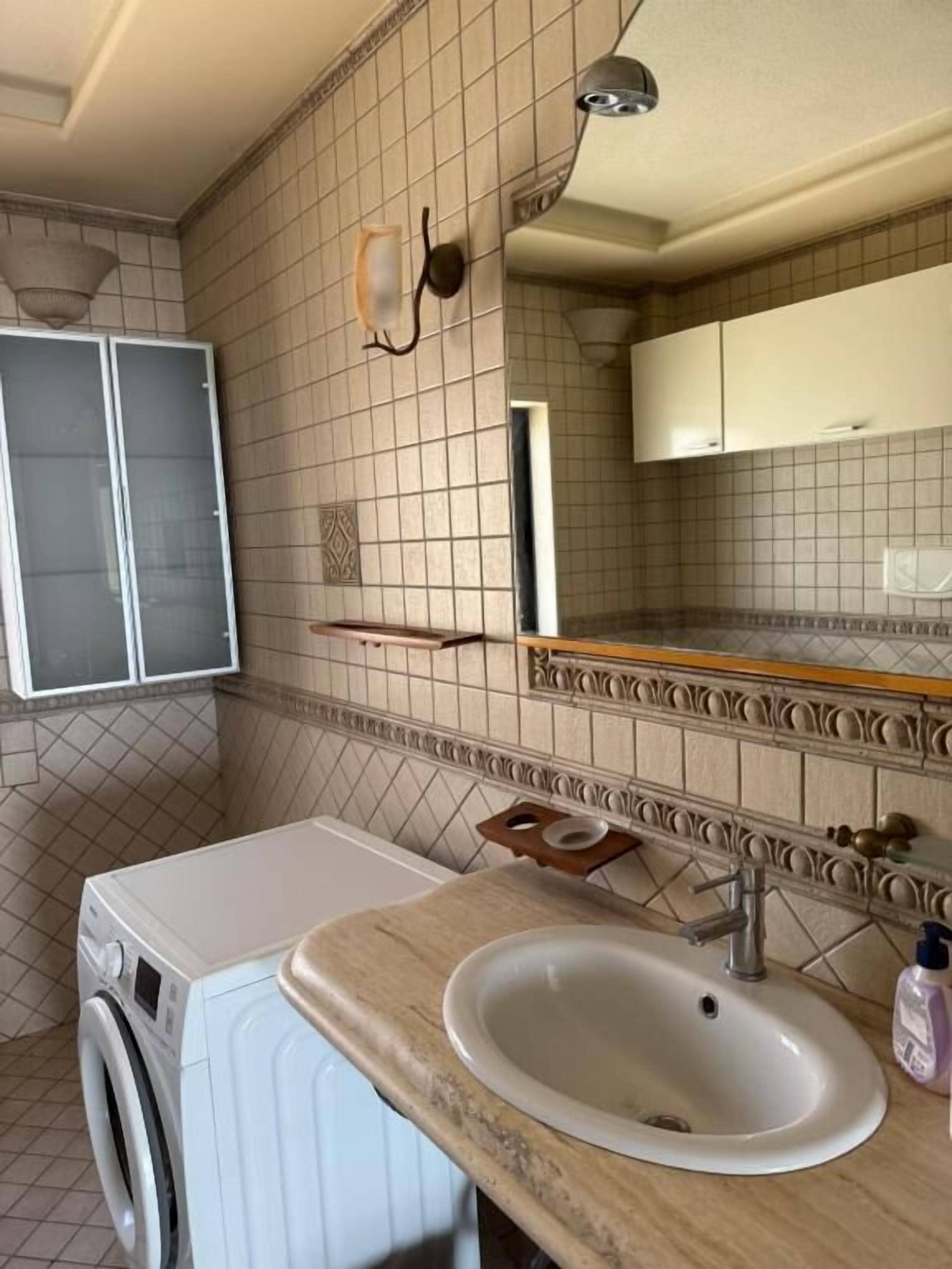 Ett litet badrum med tvättmaskin, handfat och spegel.