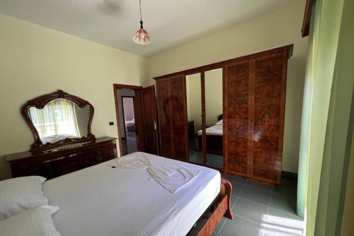 A bedroom with a large bed, a wooden wardrobe, and a mirror on a dresser.