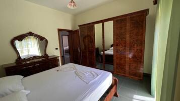 A bedroom with a large bed, a wooden wardrobe, and a mirror on a dresser.