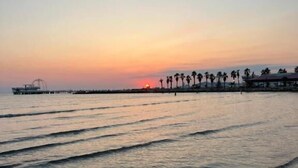 Une plage aux eaux calmes, une jetée et des palmiers au coucher du soleil.