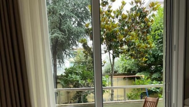 Une chambre d’hôtel avec un lit, une chaise en bois et une vue sur un balcon agrémenté de verdure.