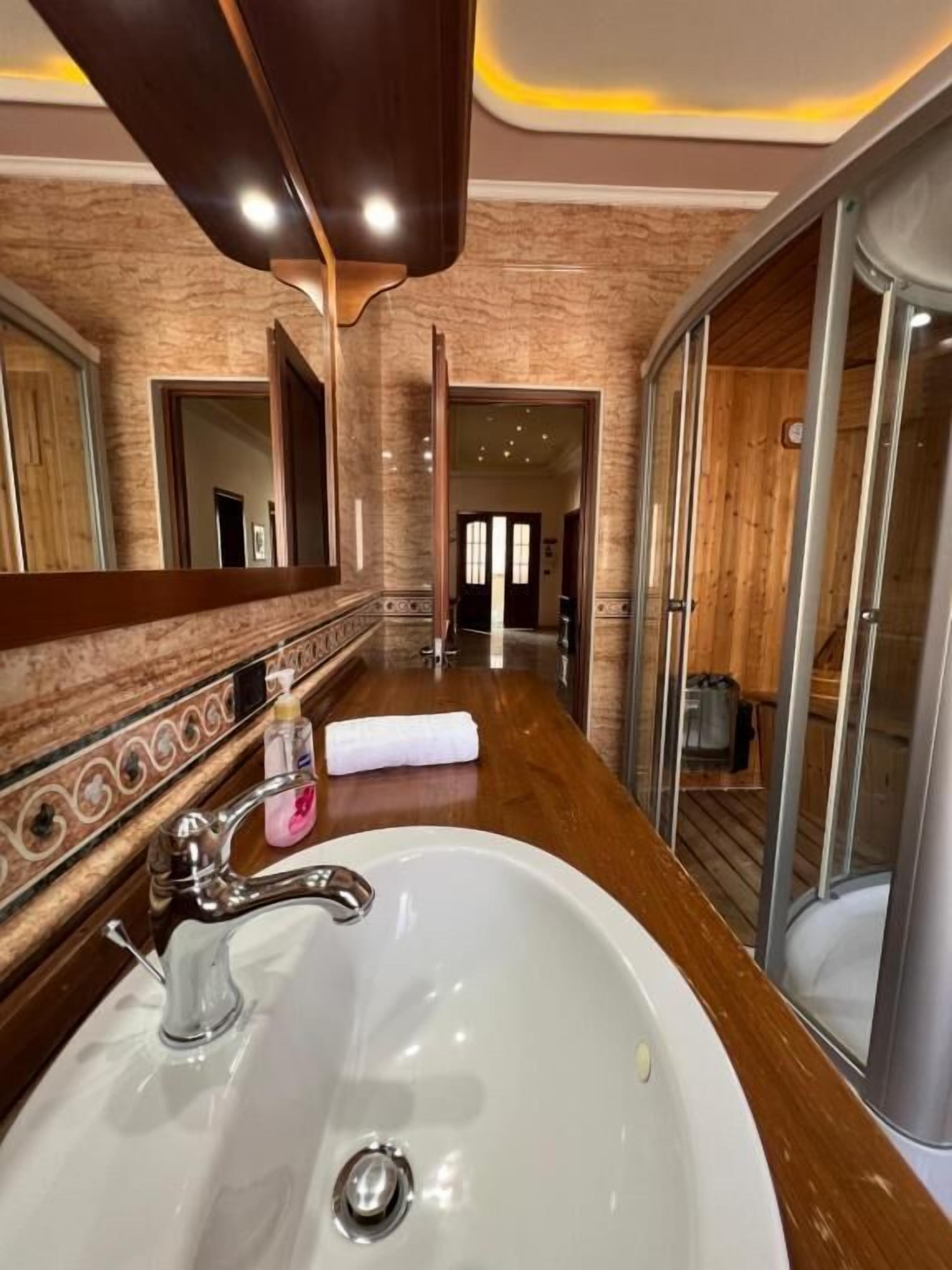 A bathroom with a large mirror, a white sink, and a wooden vanity.