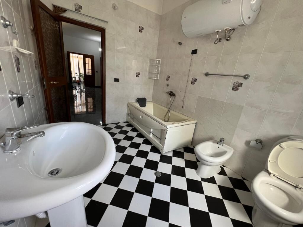 A bathroom with a checkered floor, a sink, a bidet, and a toilet.