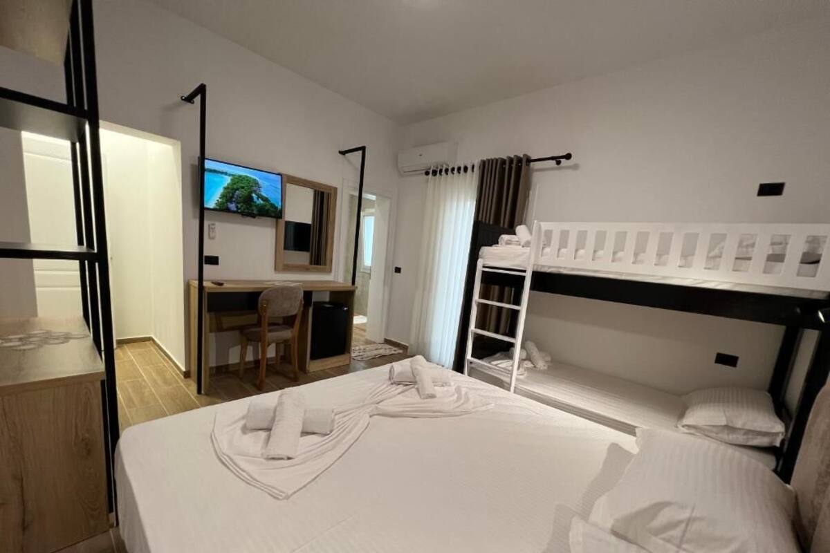 A hotel room with a bunk bed, a desk with a chair, a TV, and a bed with neatly folded towels.