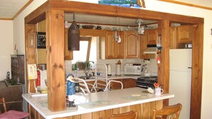 A kitchen with wooden cabinets, a white refrigerator, a stove, and a microwave. There are two wooden chairs and a small table.