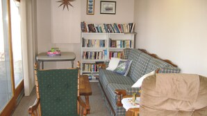 Una sala de estar acogedora con un sillón verde, un sofá a cuadros, una mesa de centro de madera y una estantería llena de libros.
