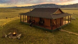 Una cabaña rústica con un porche, un hogar a leña y vistas a montañas distantes.