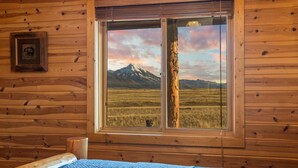 Una habitación de cabaña de madera con un ventanal grande que da a un paisaje montañoso.