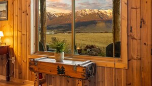 Interior de una cabaña de madera con un ventanal grande que da a un paisaje montañoso.