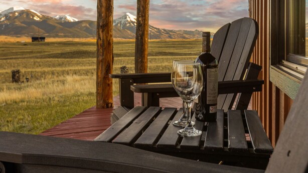 Una terraza de madera con una copa de vino y una botella, con vistas a un paisaje montañoso.