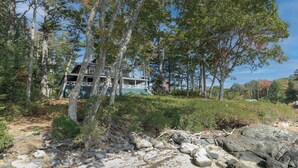 A cabin surrounded by dense forest, with a rocky shoreline in the foreground.