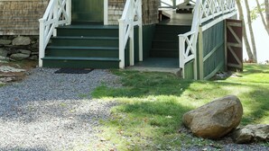 A two-story wooden house with a porch, green shutters, and a stone foundation.