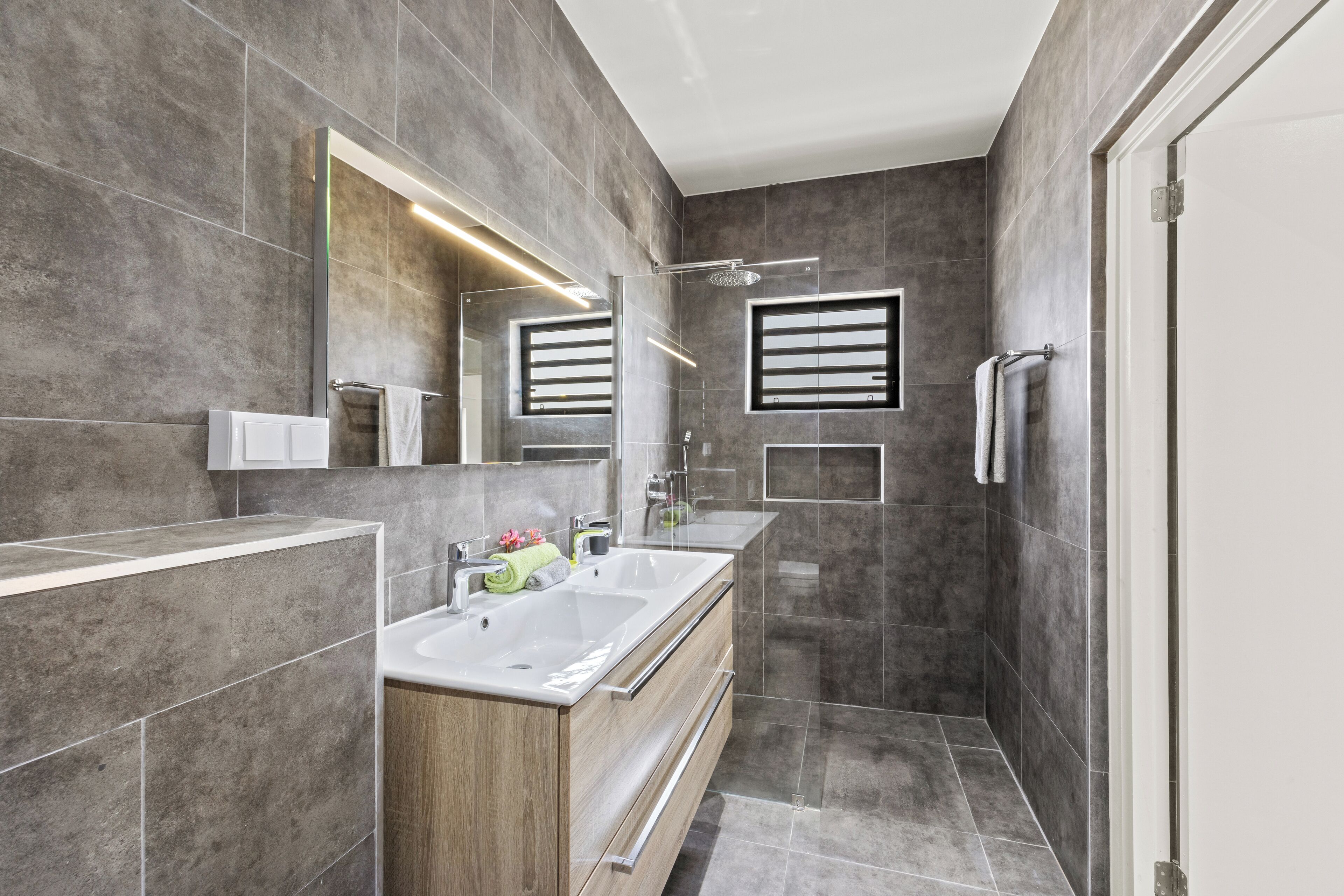 Un baño moderno con un espejo grande, dos lavamanos, una ducha y una cabina de ducha.