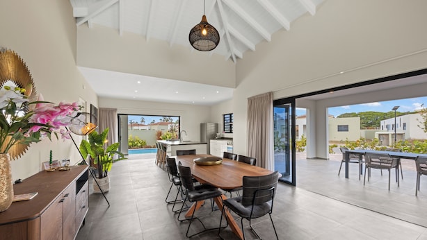 A spacious dining area with a long wooden table and black chairs, a kitchen in the background, and a view of the outside. - Villa Amber with pool at mambo beach (Willemstad)