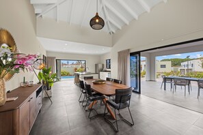 A spacious dining area with a long wooden table and black chairs, a kitchen in the background, and a view of the outside. - Villa Amber with pool at mambo beach (Willemstad)