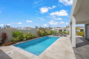 A rectangular swimming pool with a tiled deck, surrounded by various plants and a clear blue sky. - Villa Amber with pool at mambo beach (Willemstad)