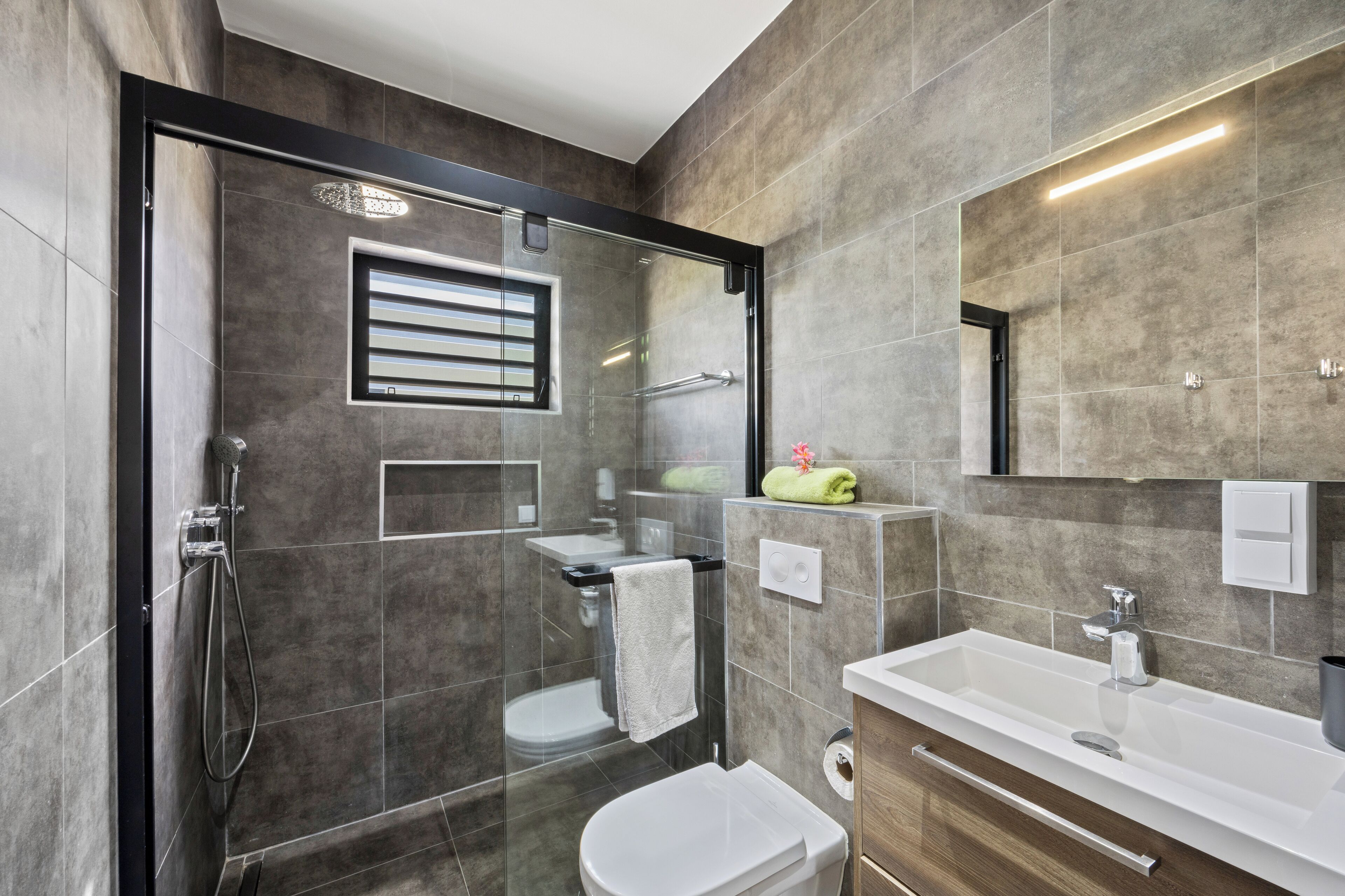 Une salle de bain moderne avec une douche à parois de verre, des toilettes blanches et un lavabo avec un miroir au-dessus.