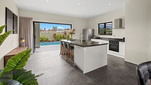 A modern kitchen with a central island, bar stools, and a view of a swimming pool. - Villa Amber with pool at mambo beach (Willemstad)