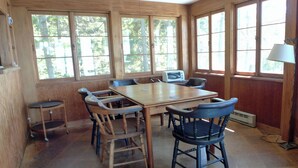 A dining area with a wooden table and chairs, large windows, and a ceiling fan.