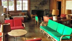 A cozy living room with red and green sofas, a round wooden table, and a fireplace.