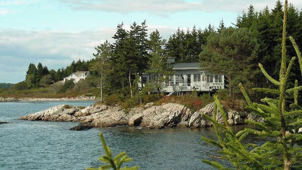 A coastal property with a large house surrounded by trees and rocky shoreline.